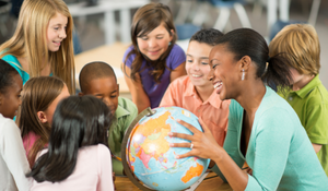 Diverse students looking at a globe with their teacher in the classroom